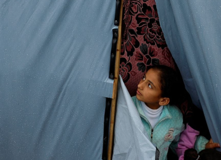 Seorang anak Palestina melihat keluar dari tenda setelah hujan, di tengah konflik yang sedang berlangsung antara Israel dan kelompok Islam Palestina Hamas, di Khan Younis di selatan Jalur Gaza, 19 November 2023. REUTERS/Mohammed Salem Memperoleh Hak Lisensi