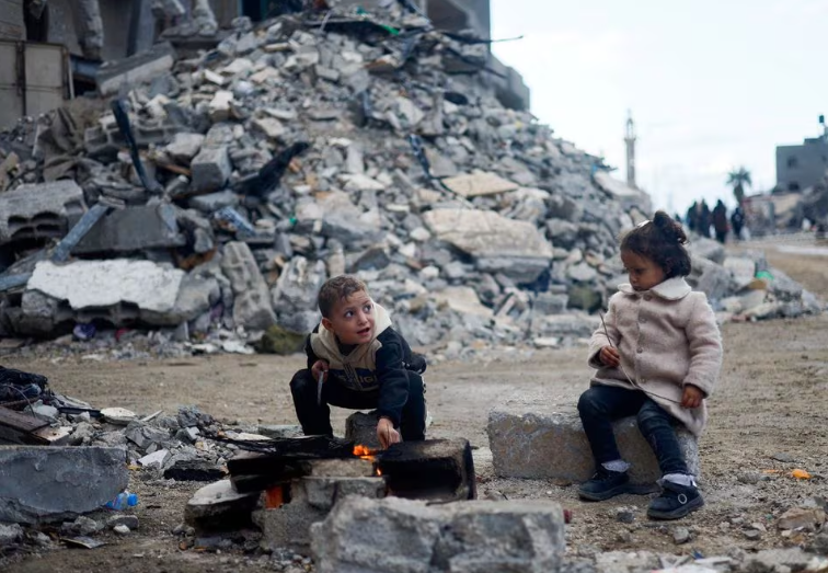 Anak-anak Palestina duduk di dekat api di samping puing-puing rumah yang terkena serangan Israel selama konflik, di tengah gencatan senjata sementara antara Hamas dan Israel, di Khan Younis di selatan Jalur Gaza 27 November 2023. REUTERS /Mohammed Salem/ File foto Memperoleh Hak Lisensi