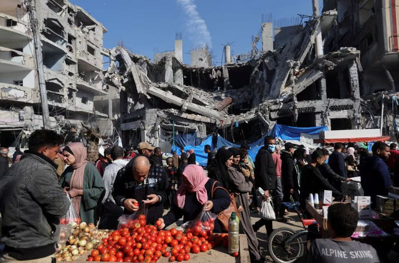 Warga Palestina berbelanja di pasar terbuka dekat reruntuhan rumah dan bangunan yang hancur akibat serangan Israel selama konflik, di tengah gencatan senjata sementara antara Hamas dan Israel, di kamp pengungsi Nuseirat di Jalur Gaza tengah 30 November. REUTERS /Ibraheem Abu Mustafa Memperoleh Hak Lisensi